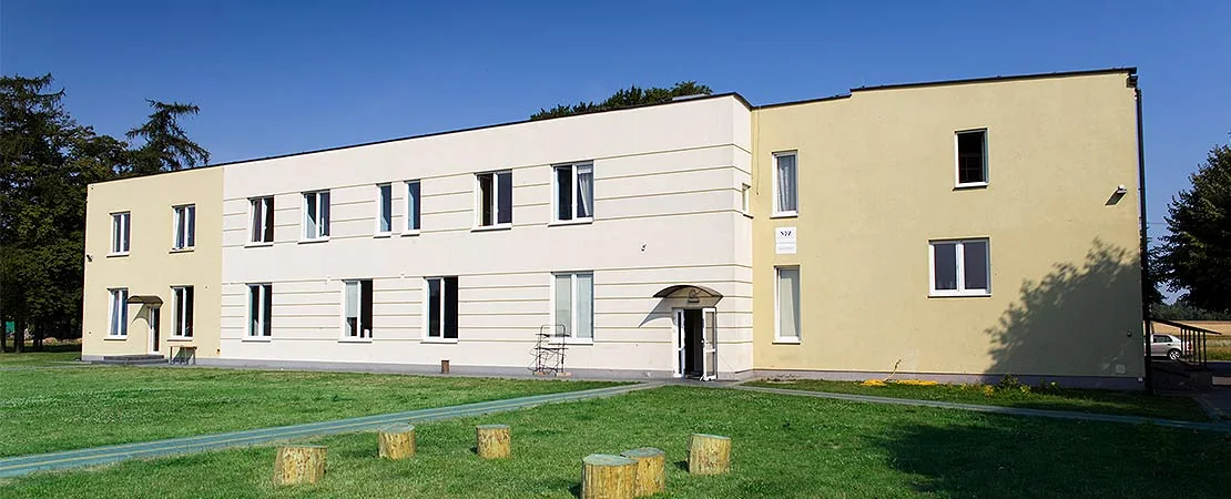 Budynek ośrodka TO TU w Karnicach z jasną elewacją i żółtym wejściem.