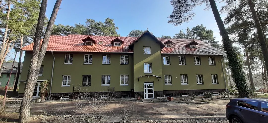 Budynek na terenie szpitala w Ciborzu z zieloną elewacją i czerwonym dachem.