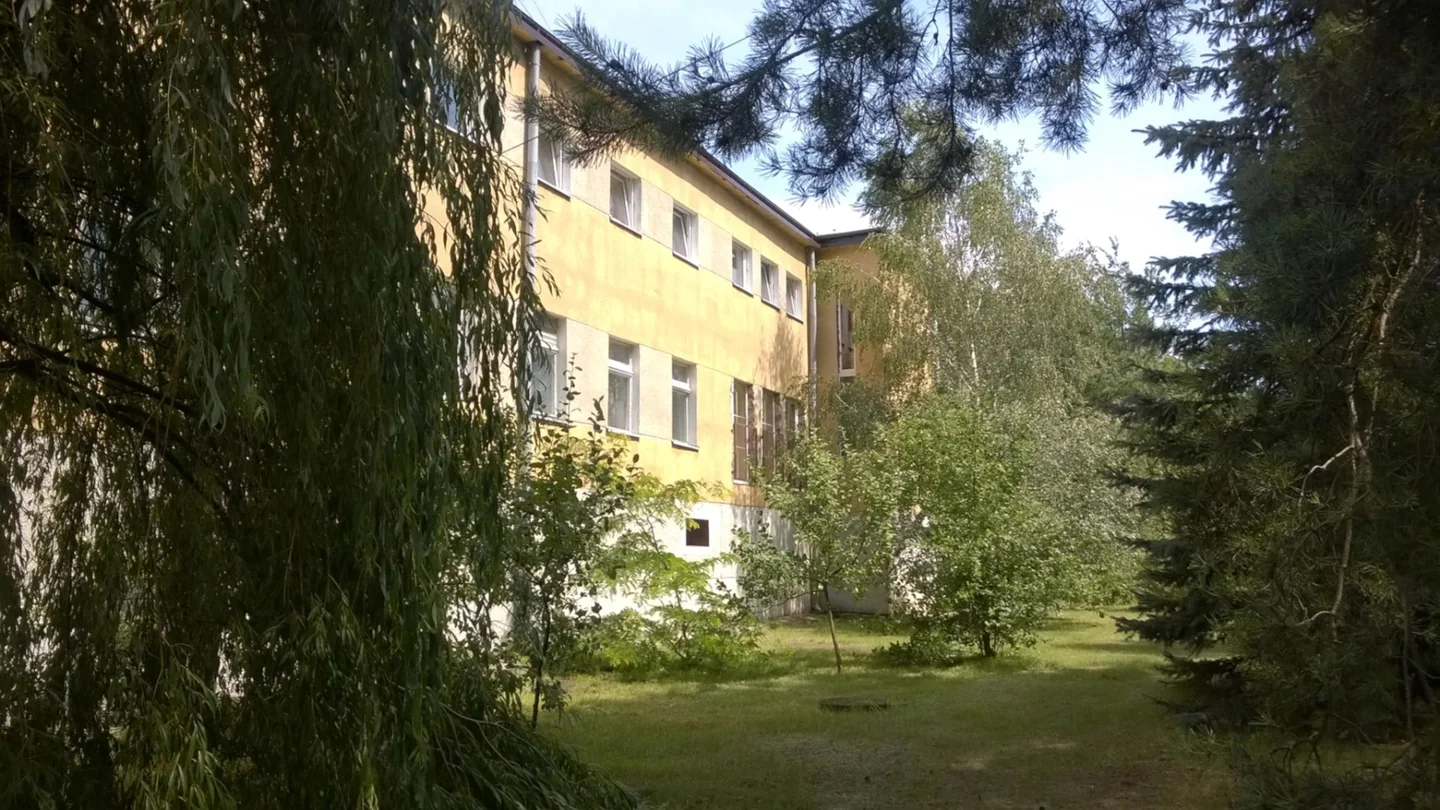 Budynek ośrodka MONAR w Lipiance widziany od strony ogrodu, z żółtą elewacją i drzewami.