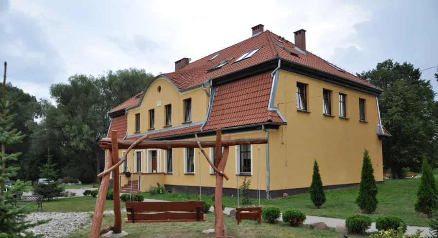 Żółty budynek ośrodka Doren i huśtawka w ogrodzie w Różewcu koło Węgorzewa