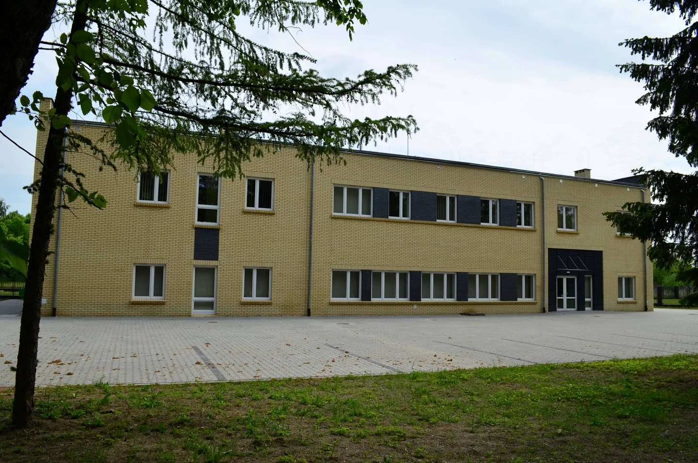 Budynek oddziału 25a leczenia uzależnień szpitala Dziekanka w Gnieźnie, z jasną ceglaną elewacją i placem przed wejściem.