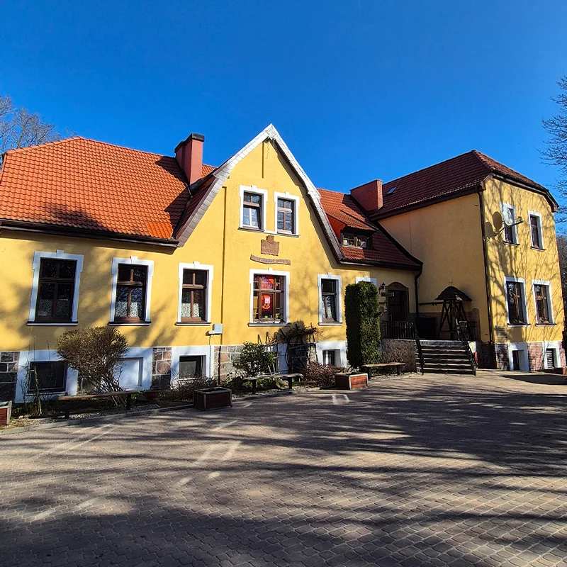 Budynek ośrodka MONAR Marianówek we Wszemierzycach, z żółtą elewacją, czerwonym dachem i dziedzińcem.