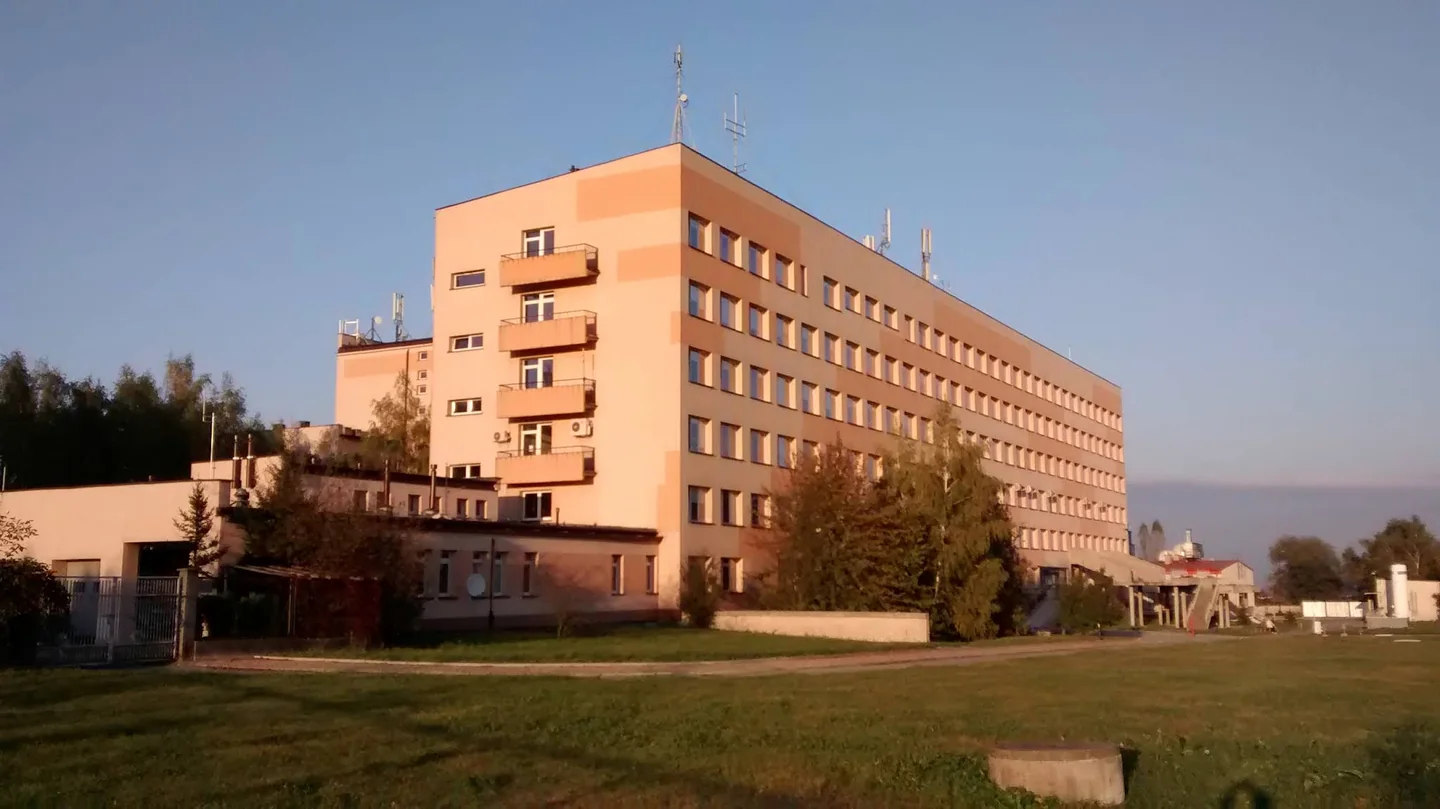 Budynek szpitala w Brzesku przy ulicy Kościuszki 68, z trawnikiem i drzewami przed elewacją.