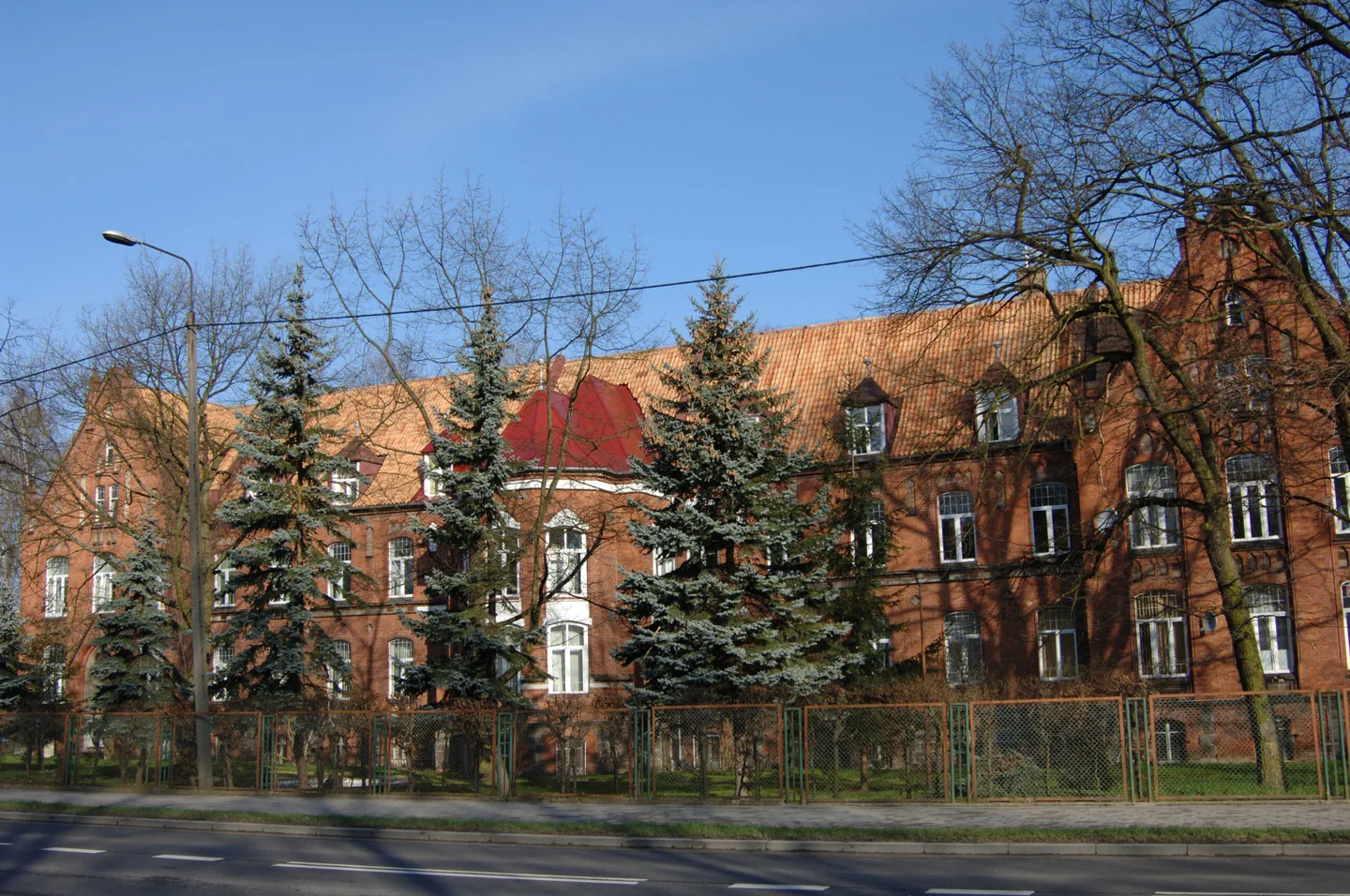 Budynek kompleksu szpitalnego w Lidzbarku Warmińskim z ceglaną elewacją i czerwonym dachem.