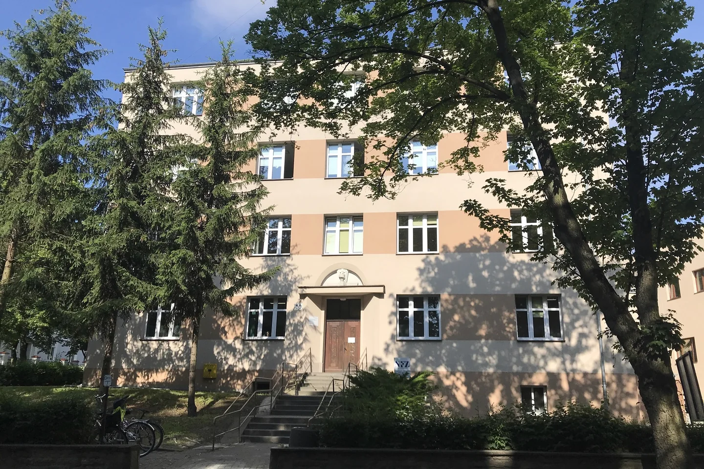 Budynek przychodni SPZOZ w Mogilnie przy ul. Kościuszki 10, z wejściem po schodach i drzewami przed elewacją.