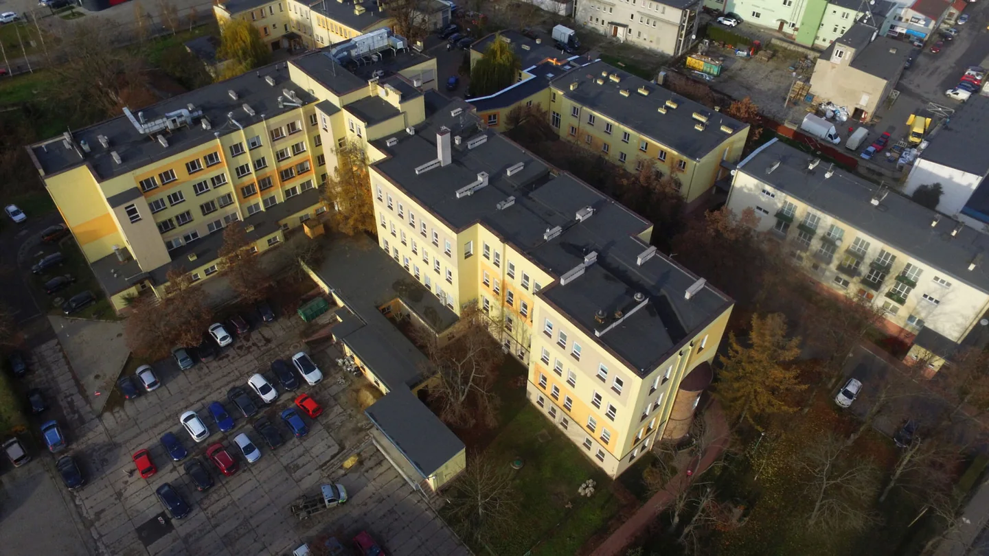 Budynki Pałuckiego Centrum Zdrowia w Żninie widziane z góry, z parkingiem i drzewami.