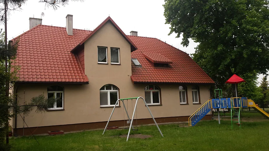 Budynek MOPTUiW w Wieruszowie z czerwonym dachem i zielonym terenem przed ośrodkiem.