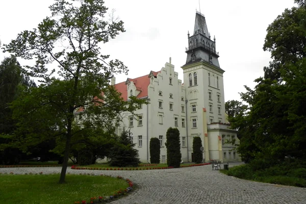 Budynek Ośrodka Leczenia Odwykowego w Woskowicach Małych, z wieżą i zielenią przed wejściem.